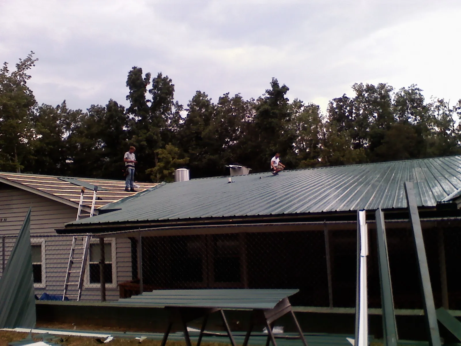 Two roofers installing green metal panels above a covered porch in Incline Village